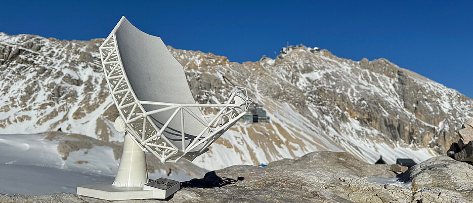 Modell des Wetterstein Millimeter Teleskops an einem der möglichen Standorte am Zugspitzplatt. Die Umweltforschungsstation ist im Hintergrund sichtbar, rund dreihundert Höhenmeter unterhalb des Gipfels der Zugspitze.